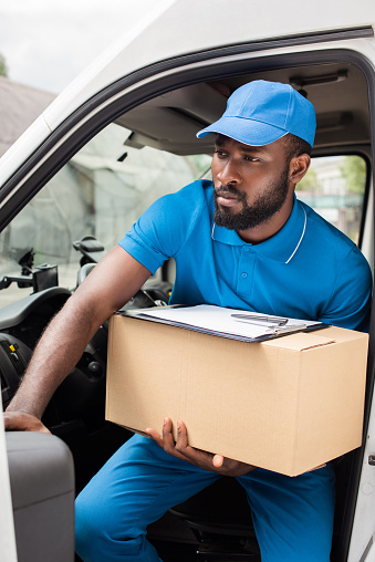 african american delivery man going out from car with box